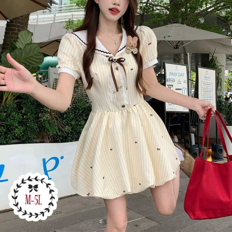 大きいサイズ レディースのクリームイエロー半袖ミニワンピース。ストライプと小リボン柄、セーラー襟とブラウンリボン、ふんわり裾のガーリーデザイン着用例