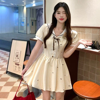 大きいサイズ レディースのクリームイエロー半袖ミニワンピース。ストライプと小リボン柄、セーラー襟とブラウンリボン、ふんわり裾のガーリーデザイン着用例